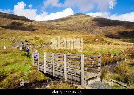 Fußgängerbrücke über die berggebiete Stream mit Wanderer Wandern auf Pfad unten Yr Aran in Snowdonia National Park. Beddgelert, Gwynedd, Wales, Großbritannien, Großbritannien Stockfoto