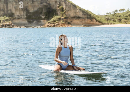 Gerne Frau sitzt auf Surfbrett im Meer Stockfoto