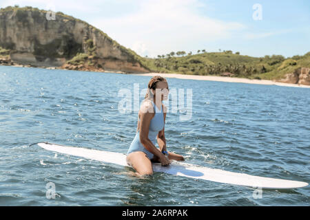 Gerne Frau sitzt auf Surfbrett im Meer Stockfoto