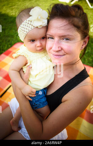 Portrait Junge Mutter holding Cute Baby Mädchen in gelbes Band und Kleid. Sonnigen Sommertag im Freien. Stockfoto