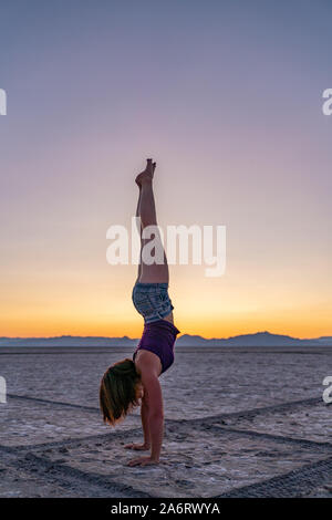 Schöne Frau macht Handstand während des Sonnenuntergangs in Bonneville Salt Flats Stockfoto