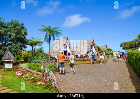 Santana, Insel Madeira, Portugal - Sep 24, 2019: Touristen bewundern Traditionelle bunte Häuser. Eine der wichtigsten Sehenswürdigkeiten in Madeira, portugiesische Erbe. Palmen, bunte Blumen, sonnigen Tag. Stockfoto