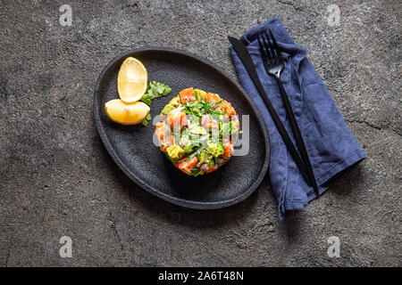 Peruanische NIKKEI ESSEN. Lachs, Avocado ceviche auf schwarze Platte, schwarzen Hintergrund, Ansicht von oben Stockfoto