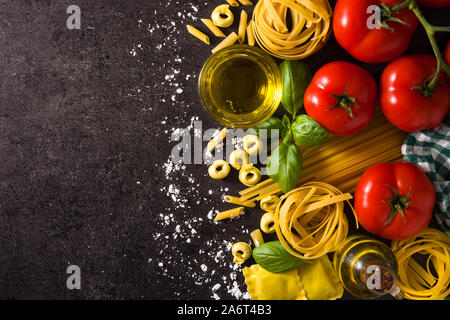 Italienische Pasta und Zutaten. Ravioli, Nudeln, Spaghetti, Tortellini, Tomaten und Basilikum auf schwarzem Hintergrund. Ansicht von oben kopieren Raum Stockfoto