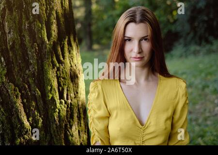 Porträt der rothaarige Junge Frau, die in der Nähe von Tree Stockfoto