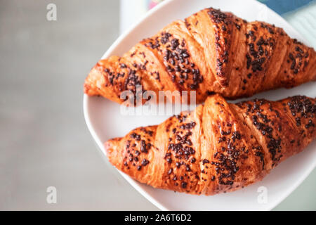 Frisch gebackene Croissants mit Schokolade, Chips in eine weiße Platte auf einem Glastisch im Wohnzimmer. Stockfoto