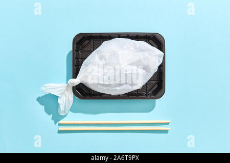 Weiße Plastiktüte in Form von Fisch auf den Teller, Essstäbchen aus Holz auf einem Pastell-blaue Hintergrund mit harten Schatten, Platz für Text. Umwelt pollut Stockfoto