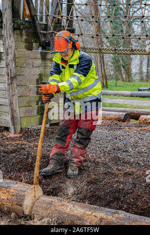 Junge Holzfäller arbeiten mit einer Axt auf einen Spielplatz, einen Baumstamm für das Schneiden mit Kettensägen in den regnerischen Tag. Stockfoto