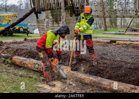 Junge Holzfäller arbeiten auf einem Spielplatz, schneiden Baumstamm mit Kettensägen in den regnerischen Tag. Stockfoto