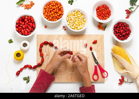 Kind macht die Kette aus roten Hagebutten Beeren. Der Herbst schmuck Dekorationen. Stockfoto