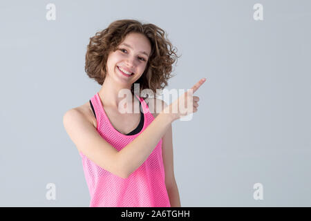 Junge schöne Frau mit lockigem Haar zeigt auf die Seite in Sportkleidung für Fitness gekleidet. Stockfoto