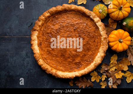 Blick von oben auf eine traditionelle Thanksgiving Kürbiskuchen auf einem urigen blau Holztisch mit kleinen Kürbisse und trockenen Blättern. Stockfoto