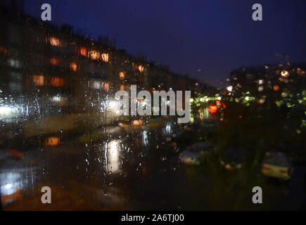 Nacht regnerischen sityscape außerhalb der Scheibe - Defokussierten verschwommenen Hintergrund mit Wassertropfen auf Glas, Bokeh der Nacht beleuchtung, geparkte Autos. Mela Stockfoto
