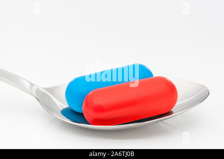 Blaue und rote Kapseln auf dem Löffel. Medicare, NHS / National Health Service, Red pilled, Blue pilled, Drogenmangel, richtig falsch, Persönliche Entscheidung. Stockfoto
