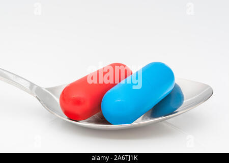 Blaue und rote Kapseln auf dem Löffel. Medicare, NHS / National Health Service, Red pilled, Blue pilled, Drogenmangel, richtig falsch, Persönliche Entscheidung. Stockfoto