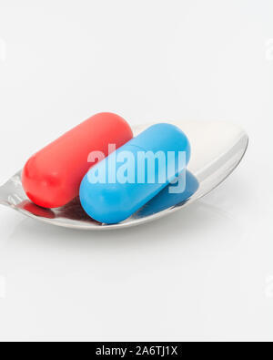 Blaue und rote Kapseln auf dem Löffel. Medicare, NHS / National Health Service, Red pilled, Blue pilled, Drogenmangel, richtig falsch, Persönliche Entscheidung. Stockfoto