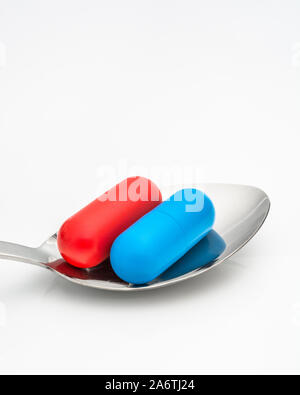 Blaue und rote Kapseln auf dem Löffel. Medicare, NHS / National Health Service, Red pilled, Blue pilled, Drogenmangel, richtig falsch, Persönliche Entscheidung. Stockfoto