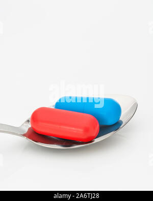 Blaue und rote Kapseln auf dem Löffel. Medicare, NHS / National Health Service, Red pilled, Blue pilled, Drogenmangel, richtig falsch, Persönliche Entscheidung. Stockfoto
