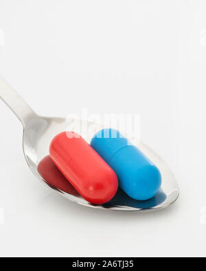 Blaue und rote Kapseln auf dem Löffel. Medicare, NHS / National Health Service, Red pilled, Blue pilled, Drogenmangel, richtig falsch, Persönliche Entscheidung. Stockfoto