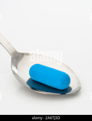 Blaue Kapsel auf Löffel. Medicare, NHS/National Health Service, Medikation, blaue Pille, rot Kissen blau schälte, Liberale, Konservative denken UK Stockfoto