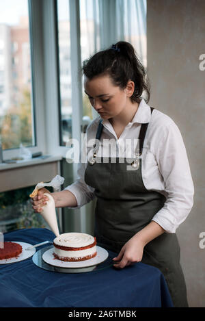 Pastry Chef drückt beige Creme auf Red Velvet Cake. Das Mädchen schmückt den Kuchen mit Sahne. Stockfoto