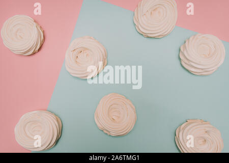 Viele weiße Baisers und Marshmallows auf Pastell rosa und blauen Hintergrund. Konzept der Bonbons, Gebäck. Stockfoto