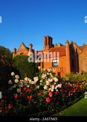 Hochformat von chenies Landsitz aus dem Westen, vom blauen Himmel umrahmt, Pastell rosa Rosen und Dahlien Sorten, 'Karma Fuschiana, Rasen und Kästchen umrandet. Stockfoto