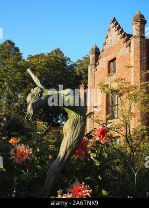 Chenies Manor Haus und Garten im Spätsommer an einem schönen Abend. hell rosa Dahlie Sorten, blauer Himmel, hohe Bäume Rahmen. Eine Skulptur erreicht. Stockfoto