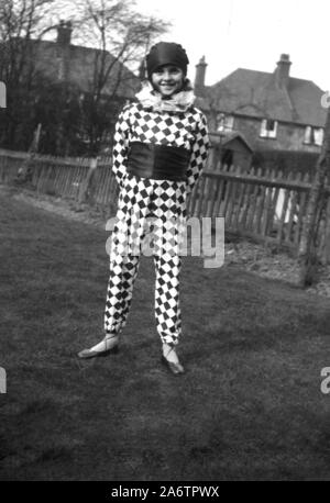 1920er Jahre, historisch, ein junges Mädchen, das draußen in einem Garten steht und ein modisches Outfit der Zeit trägt, das eines Harlequins, pierrot oder Clown, mit Hut, karierten Ärmeln und breitem Gürtel oder Kummerband, England, Großbritannien. Ein pierrot ist eine Figur des Pantomins und der italienischen Commedia dell'arte. Stockfoto
