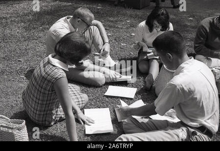 1964, historische, junge Männer und Frauen sitzen zusammen auf dem Gras auf dem Campus der University of Southern California (USC), Los Angeles, Kalifornien, USA, und schauen sich den Zeitplan der Aktivitäten für neue Studenten an. Stockfoto