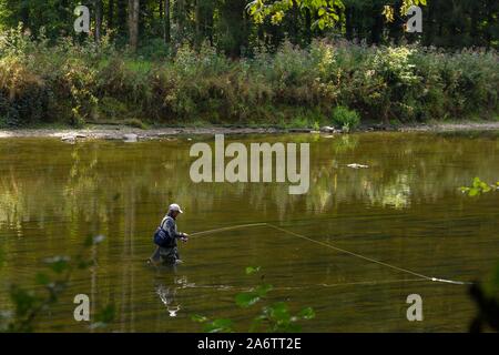 Das Porträt einer Fliege Fischer in einem Fluss. Der Fischer reeling in seinen Stab, um zu versuchen, einige Fische zu fangen. Stockfoto