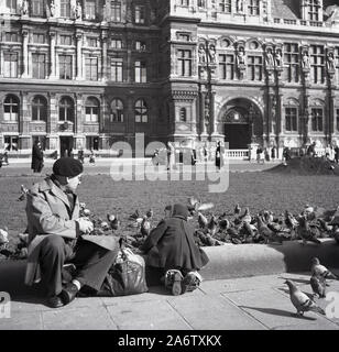 1950er Jahre, historisch, ein pariser Gentleman in Baskenmütze und Regenmantel mit seiner Enkelin, die die Tauben auf dem Platz vor dem Grand Hotel de Ville, dem Rathaus von Paris, füttert. Stockfoto