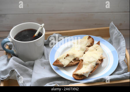 Rustikales Frühstück: Zwei heisse baguette Sandwiches mit Hähnchen Fleisch und Käse und eine Tasse schwarzen Kaffee auf einer hölzernen Fach Stockfoto