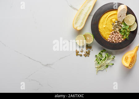 Blick von oben auf die herbstlichen Kartoffelpüree Kürbis Suppe in der Schüssel in der Nähe von Zucchini, Kürbis Samen, Sprossen und Kalk auf Marmor Oberfläche Stockfoto