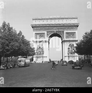 1950er Jahre, historisch, eine Dame, die ihr Fahrrad an geparkten Autos in der Nähe des Arc de Triomphe, eines der berühmten Denkmäler in Paris, Frankreich, führt. Der hohe Triumphbogen befindet sich im Zentrum des Place Charles de Gaulle an den Champs-Elysées und wurde 1836 eröffnet. Stockfoto