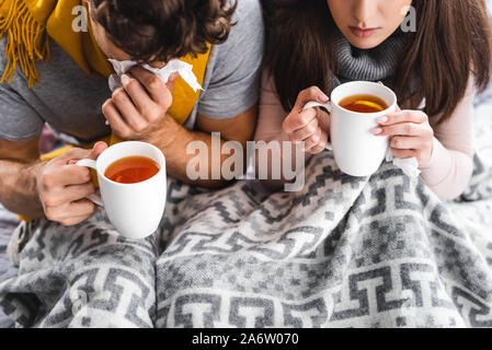 7/8-Ansicht von kranken Freundin und Freund holding Tassen und Niesen mit Tee Stockfoto