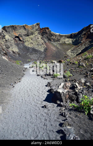 In einem Pfad, der Vulkan El Cuervo auf Lanzarote, einer der wenigen Vulkane, wo es erlaubt ist zu gehen. In den blauen Himmel ist der Mond zu sehen. Stockfoto