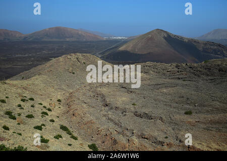 Eine karge Vulkanlandschaft auf Lanzarote, Spanien. In der Ferne sind die weißen Häuser von Mancha Blanca. Stockfoto