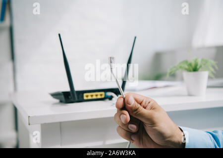 7/8-Ansicht des Geschäftsmannes holding Kabel mit Stecker in der Nähe des Routers Stockfoto