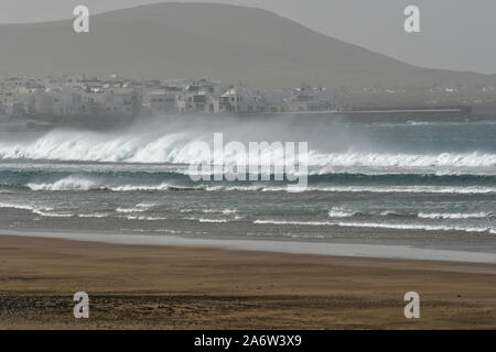 Hohe Wellen am Strand von Famara während der CALIMA Wind weht. Im Hintergrund ist die kleine Stadt Caleta de Famara. Lanzarote, Spanien. Stockfoto