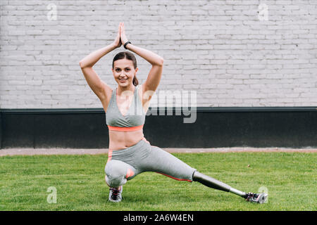 Lächelnd behinderte Sportlerin mit Prothese Yoga auf Gras Stockfoto