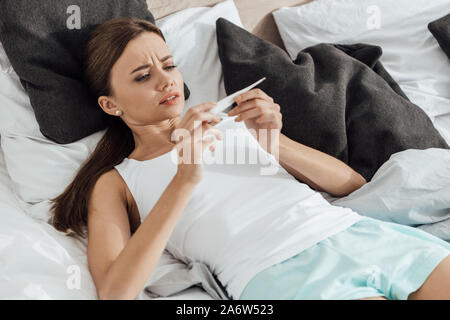 Sorgen junge Frau mit Schwangerschaft Test im Bett Stockfoto