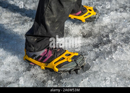 Füße in Rosa und Grau Laufschuhe mit Spikes auf gegurtet Traktion auf rutschigem Eis auf einem Gletscher zu gehen. Gewinnt auf gefrorenem Boden. Stockfoto