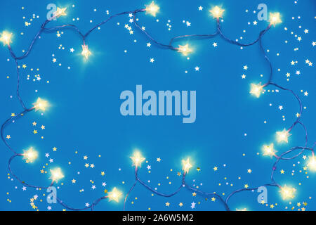 Weihnachtsbeleuchtung Rahmen mit kleinen goldenen Sternen auf blauem Hintergrund. Stockfoto