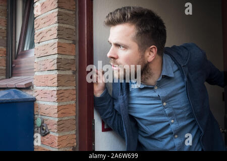 Hübscher junger Mann Öffnen der Tür auf, was sein Nachbar ist, etwas zu tun, den Verdacht. Stockfoto
