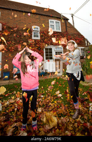 Junge Mädchen spielen mit Blättern in Garten, England Stockfoto