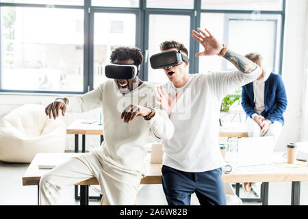 Zwei fröhlichen multikulturellen Kollegen gestikuliert während der Verwendung von VR-Headsets im Büro Stockfoto