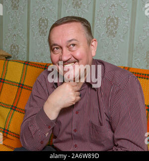 Close-up Portrait von lächelnd mit Blick bis reifen Alter Mann im gestreiften Hemd, das sitzt auf dem Sofa helle orange Plaid abgedeckt. Stockfoto