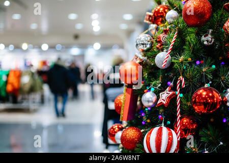 Close-up Detail elegante Weihnachtsbaum mit roten Lampen in großer supermarkt Fashion Mall Menschen kunden Silhouetten Shopping im Hintergrund. Stockfoto