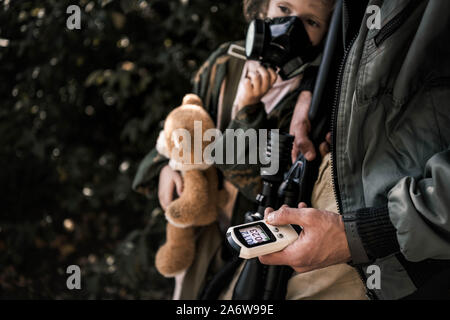 7/8-Ansicht der Mann hält Radiometer in der Nähe von Zicklein in der Gasmaske, post-apokalyptischen Konzept Stockfoto